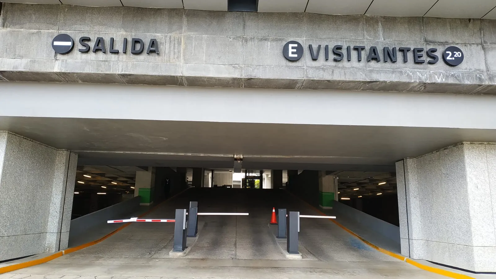 Entrada de estacionamiento con barreras vehiculares y señalización de salida y visitantes