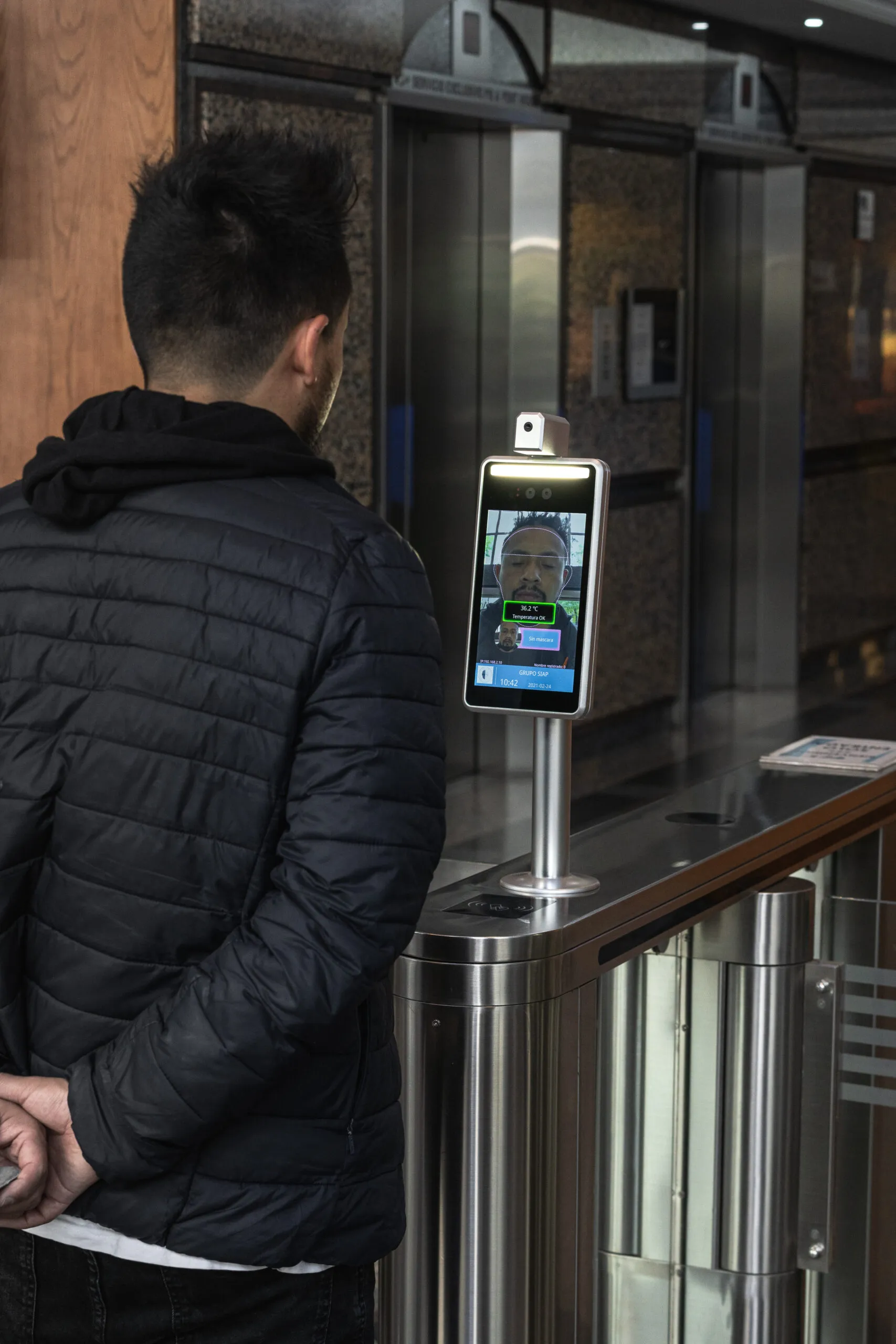 Visitante frente a un lector de reconocimiento facial en un carril de acceso